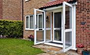 Pair of open white uPVC French doors as front doors on porch with silver letterbox and welcome mat