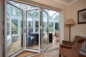 Three panel white aluminium bi-fold doors sliding open into uPVC glass conservatory dining room from the Anglian bi-fold doors range