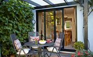 Jet Black aluminium patio doors sliding open to outside patio with black pergola and greenery